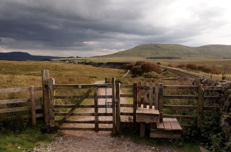 Free Image of Wooden gate opening to a scenic pathway across a rural landscape. 