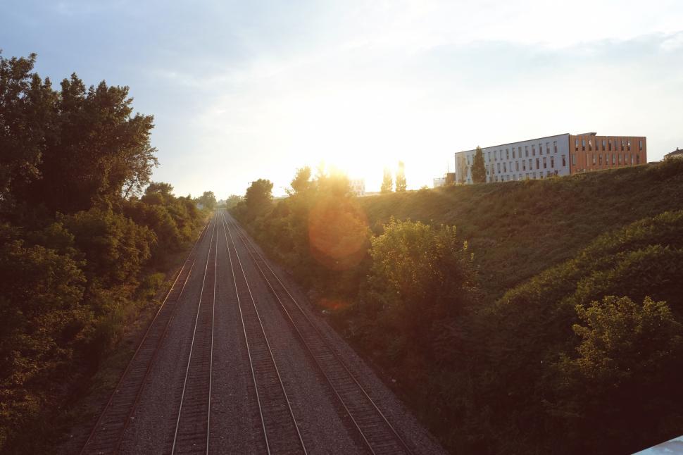Free Image of Railway tracks at sunset with nearby buildings and green trees. 