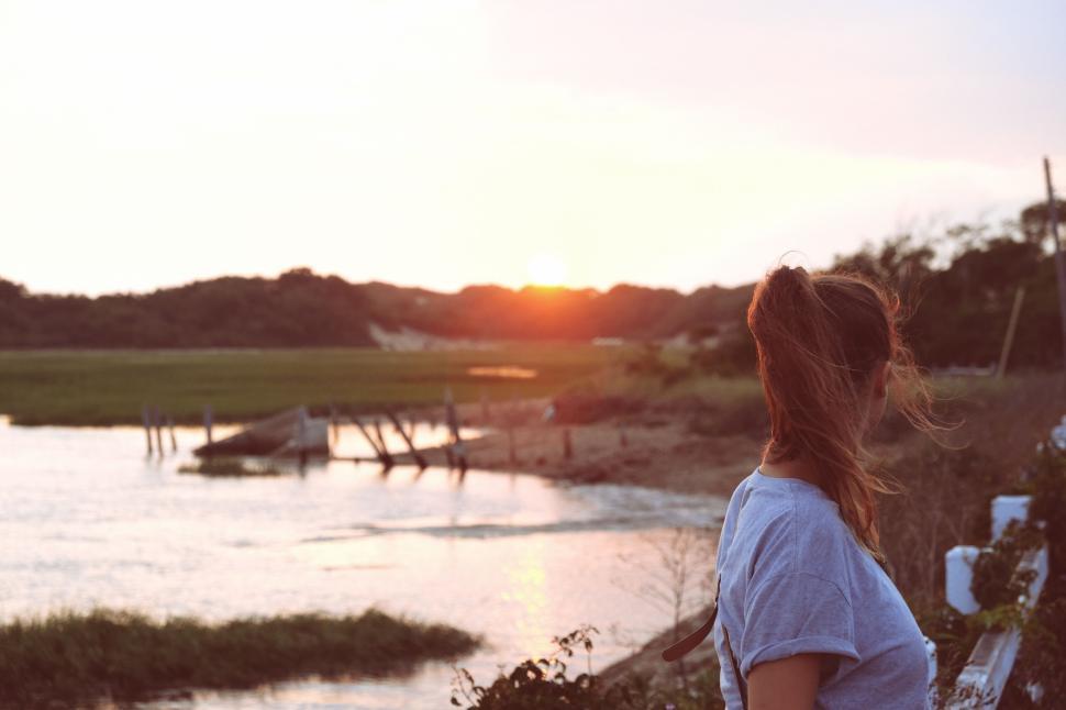 Free Image of A person watches the sunset over a peaceful coastal landscape. 