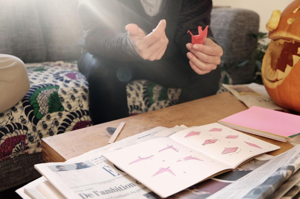 Free Image of A person crafting origami with a diagram, newspaper, and pumpkin nearby. 