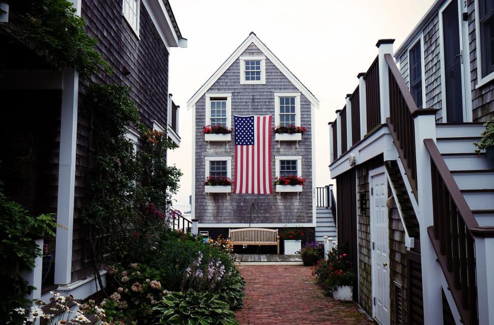 Free Image of A traditional house with an American flag between well-manicured gardens. 