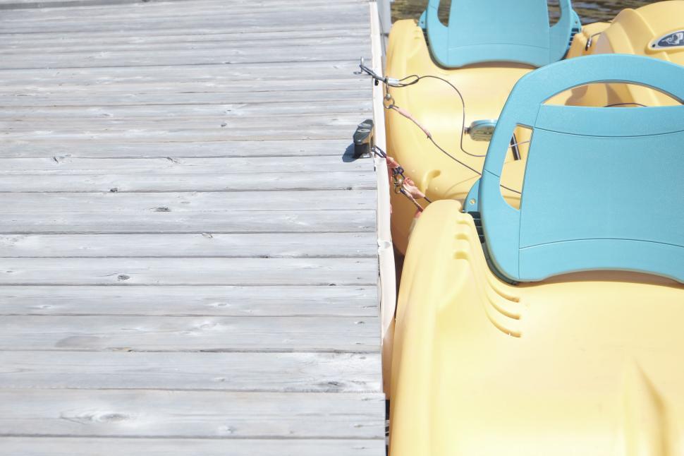 Free Image of Bright yellow pedal boats docked at wooden pier ready for use 