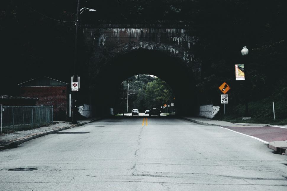 Free Image of Rural road leading through a dark tunnel with surrounding greenery. 