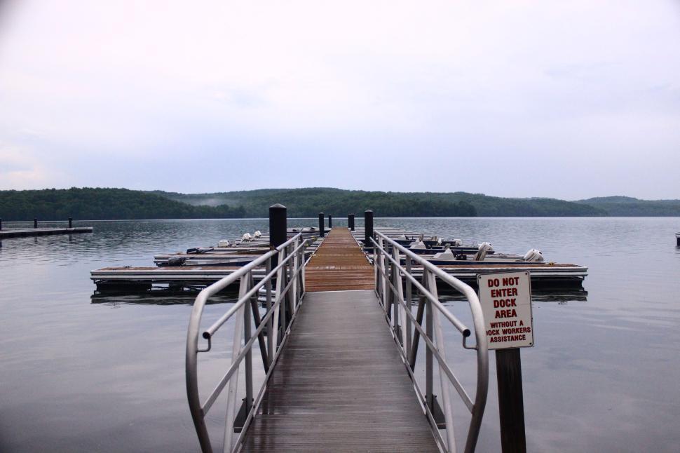 Free Image of Serene dock extending over calm lake with boats and lush landscape 