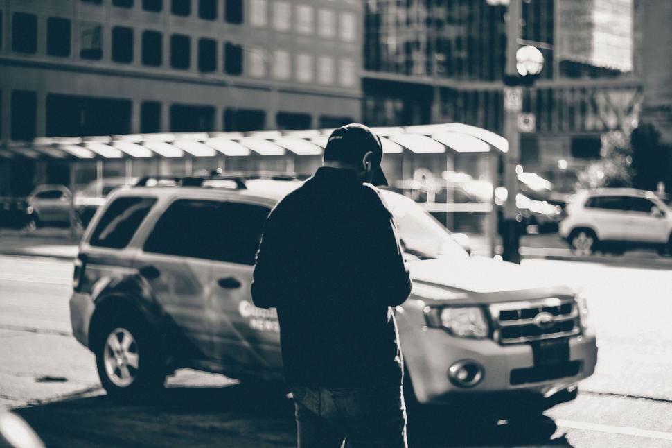 Free Image of Back view of a person standing near a vehicle on a city street. 