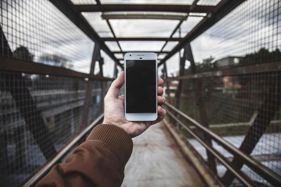 Free Image of Hand holding a smartphone on a pedestrian bridge in open air. 