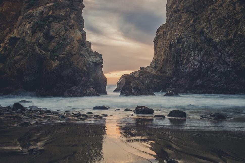 Free Image of Mysterious rocky beach passage at sunset with calm waters 