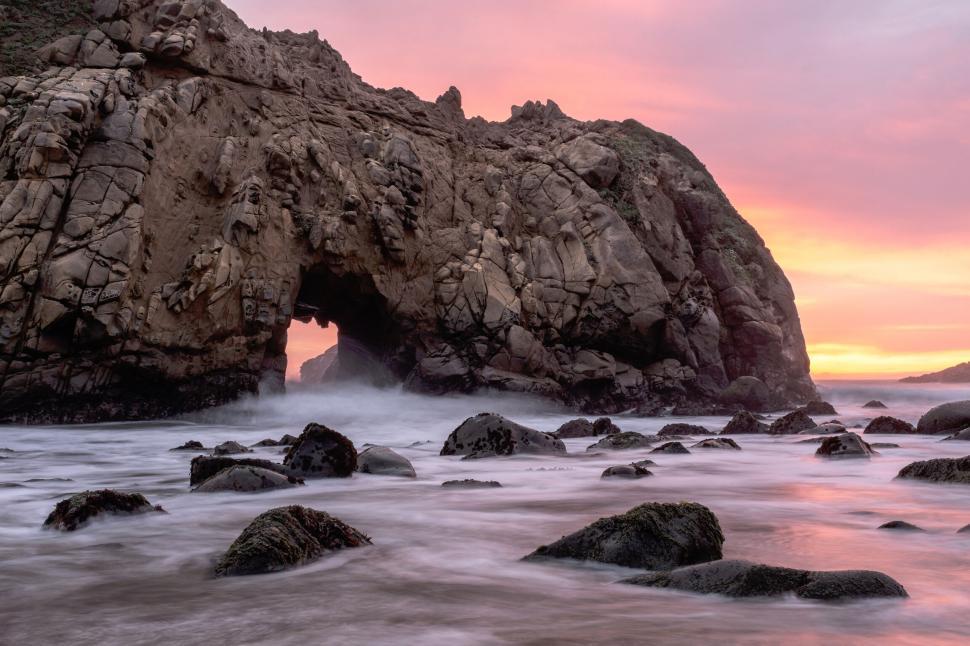 Free Image of Sunset view of rocky arch at ocean shore with pink skies above 