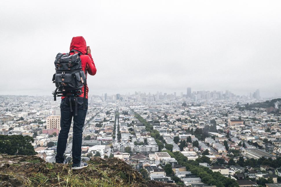 Free Image of Backpacker in red jacket photographing cityscape on misty day 