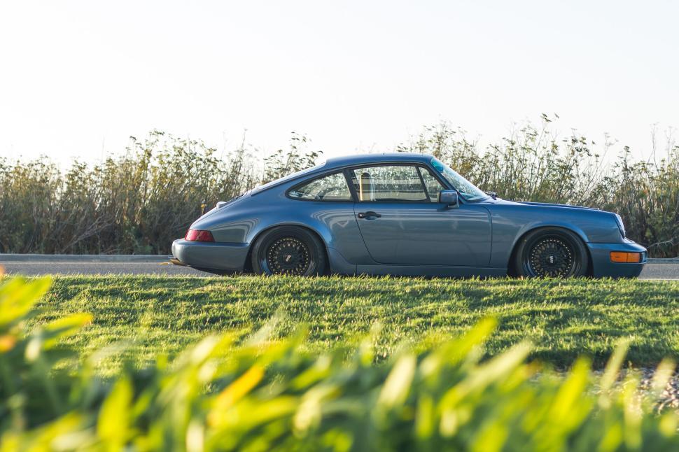 Free Image of Side view of classic grey sports car parked by green bushes 