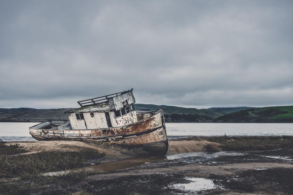 Free Image of Aged and weathered boat stranded on muddy shore by calm waters 