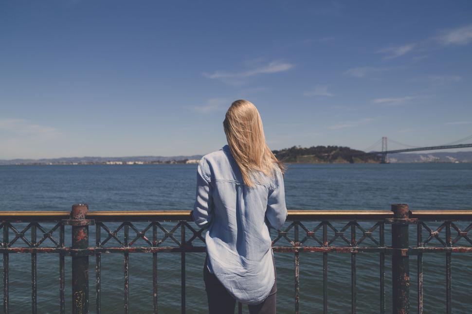 Free Image of Woman in blue shirt viewing calm ocean with distant bridge behind 