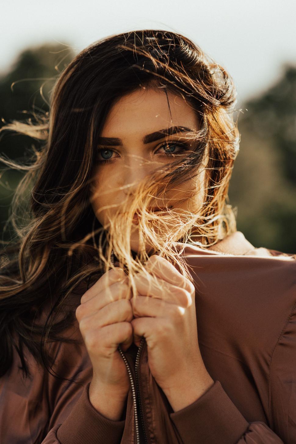 Free Image of Woman standing outside holding sweater close amidst windy weather 