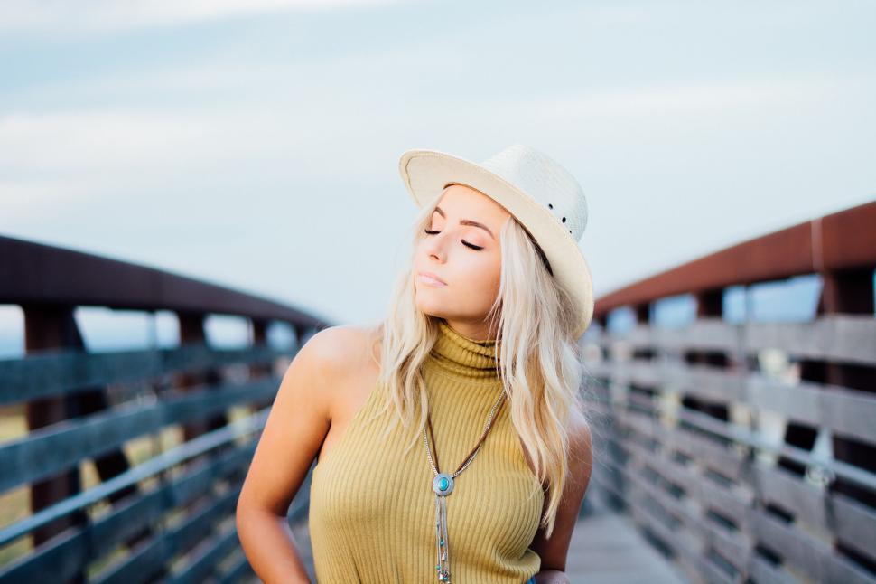 Free Image of Woman in yellow dress and hat on a wooden bridge under blue sky 