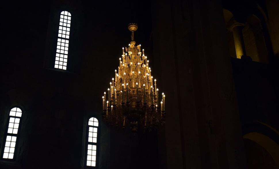 Free Image of Chandelier glowing in a dark room with sunlight through windows. 