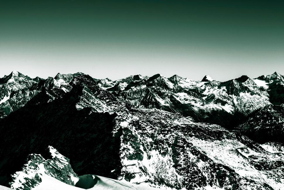 Free Image of Snowy mountain range under green sky with various peaks visible. 