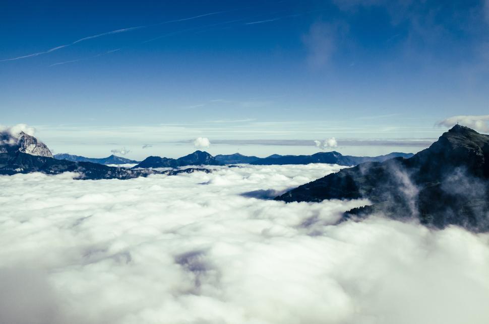 Free Image of Mountain peaks rise above a cloud-filled landscape with blue sky. 