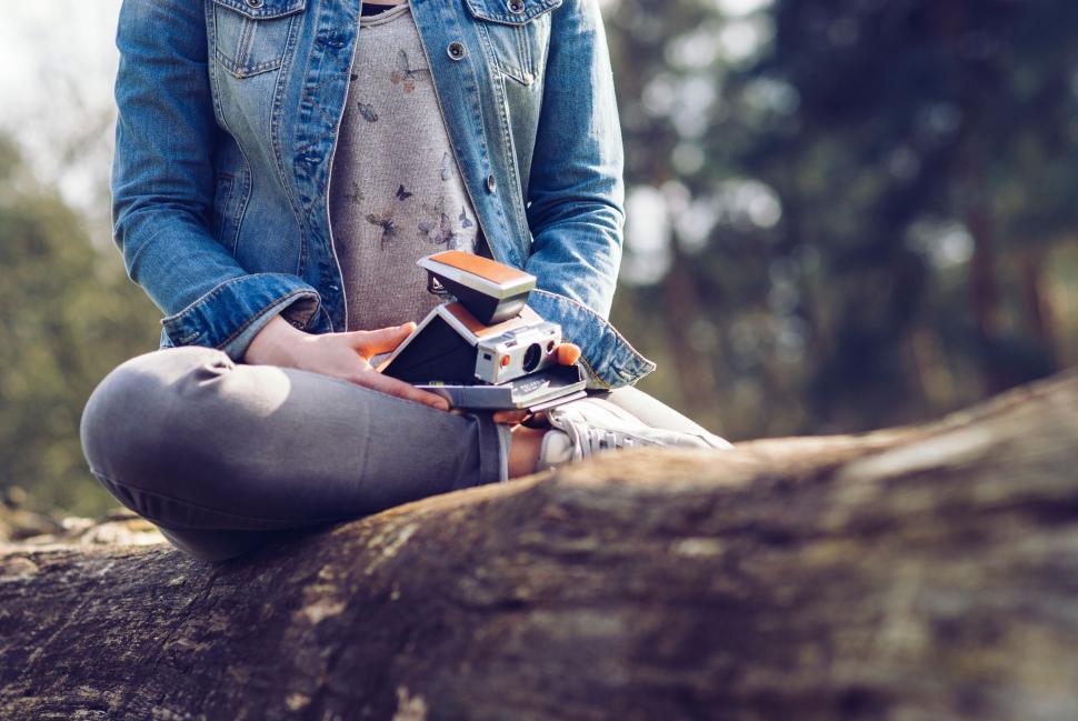 Free Image of Person holding vintage cameras while sitting on a log outdoors 