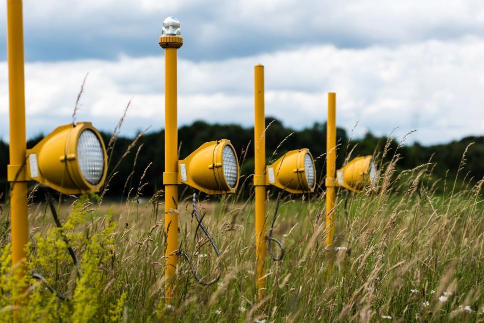 Free Image of Series of yellow lights in a grassy field under a cloudy sky 