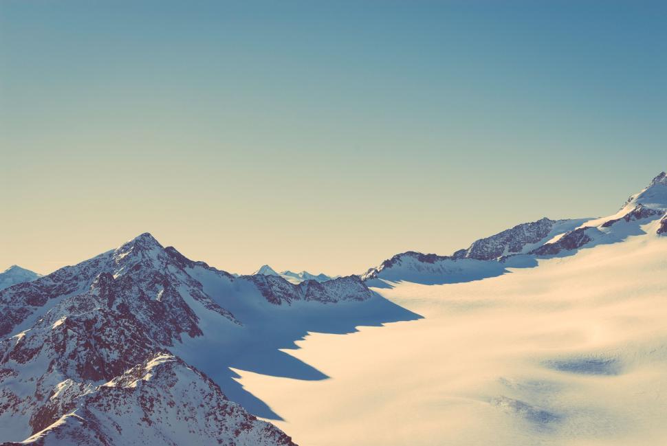 Free Image of Snow-covered mountains under clear blue sky with sunlight casting shadows 