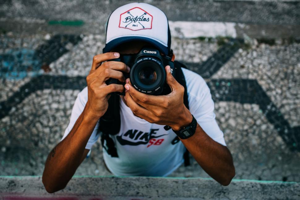 Free Image of Person with camera capturing a shot, wearing a Bragtag hat. 