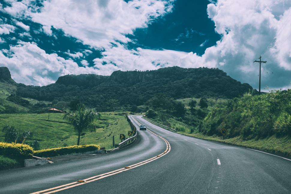 Free Image of Winding road leading into lush green mountains under a cloudy sky 