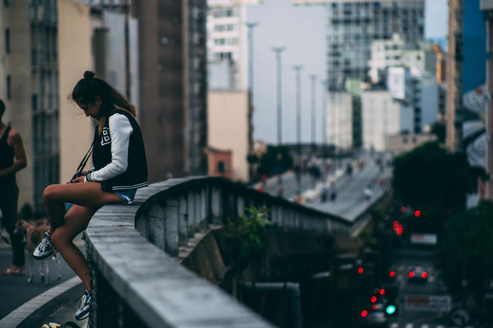Free Image of Person sitting on ledge overlooking bustling city streets below. 