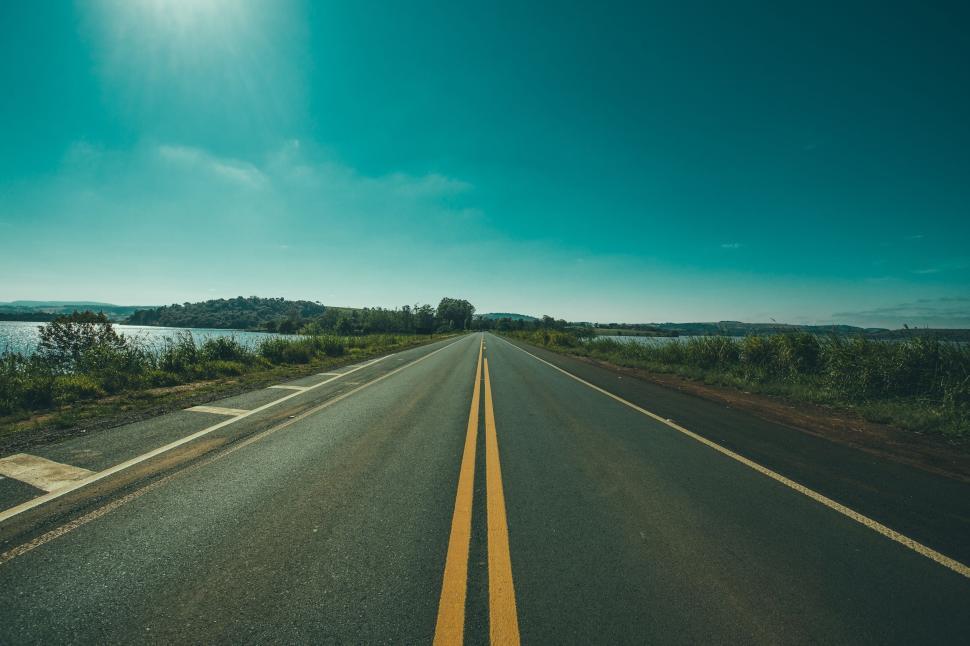 Free Image of Straight empty road with nature and water on a bright sunny day. 