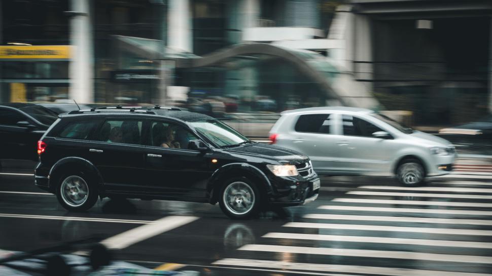 Free Image of Black SUV and white car in motion on wet street with buildings 