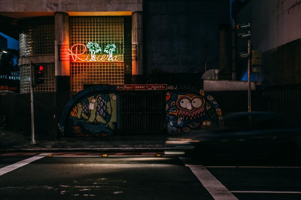 Free Image of Neon-lit street with graffiti and a car in motion at nighttime 