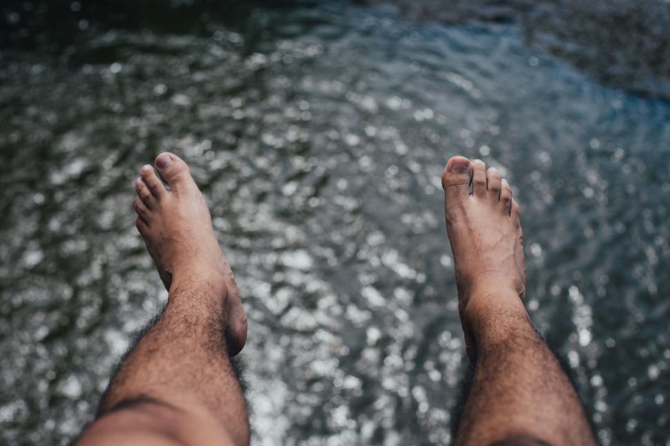 Free Image of Relaxed scene of feet dangling over water reflecting sunlight below. 