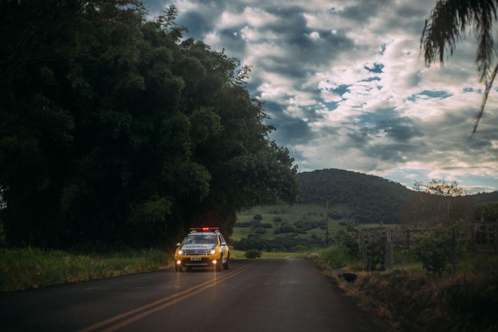 Free Image of Police car with lights on driving down a rural road at dusk 