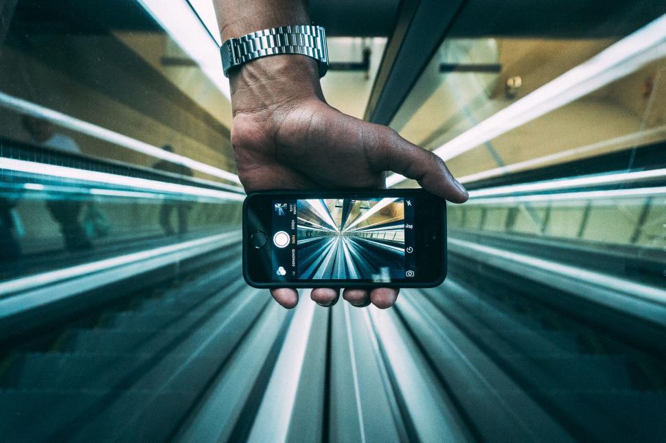 Free Image of Hand holding smartphone capturing moving escalator visual effect. 