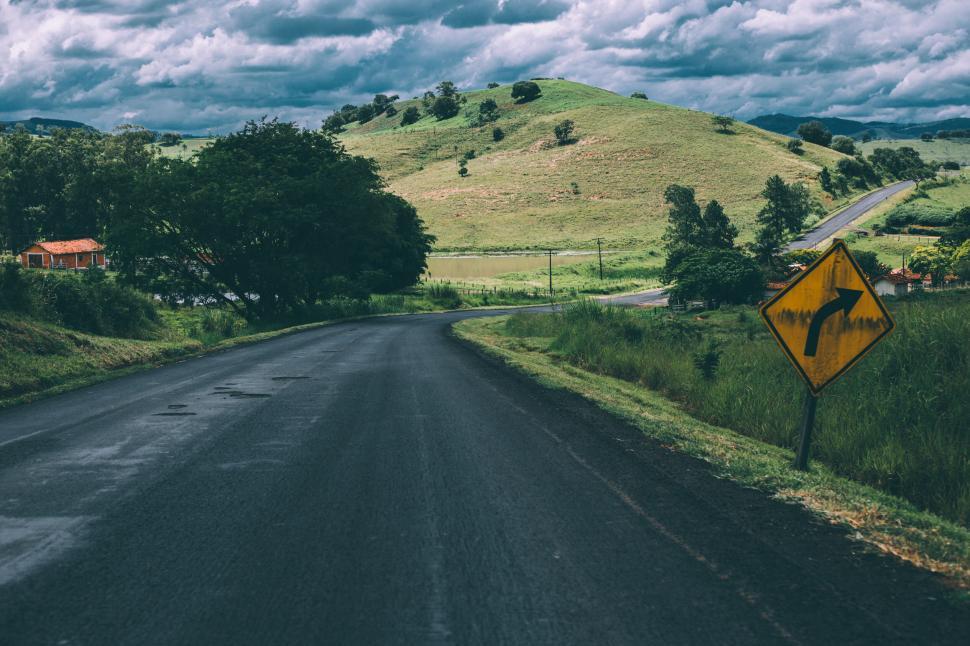 Free Image of Countryside road with green hills and turn warning road sign. 