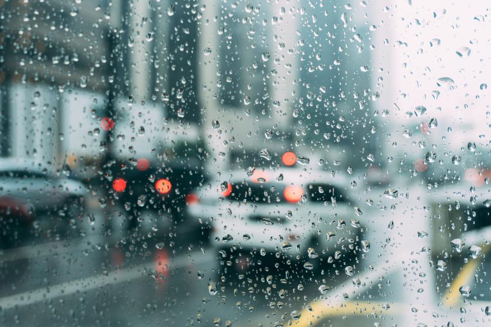 Free Image of Raindrops on window with city traffic and blurred lights behind. 