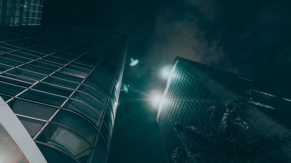 Free Image of Dramatic night view looking up at tall skyscrapers with lights. 