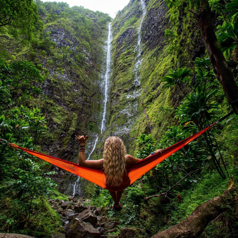 Free Image of Person relaxing on a hammock amidst lush greenery near waterfall 