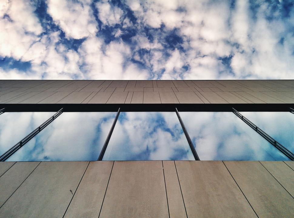 Free Image of Reflective glass building mirroring the cloudy sky above 