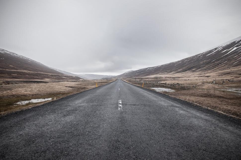 Free Image of Long empty road stretching into the distance under a cloudy sky 