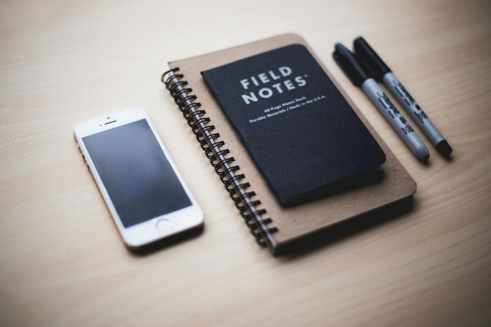 Free Image of Smartphone and notebooks on a wooden desk with pens beside it. 