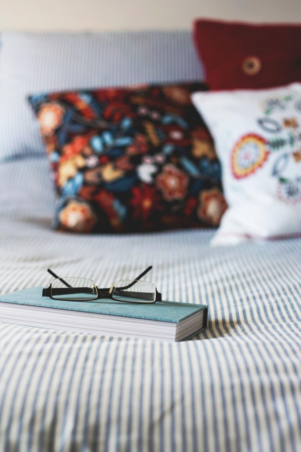 Free Image of Reading glasses on a book placed on a neatly made bed. 