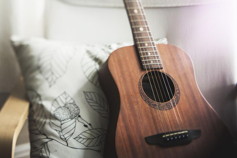Free Image of Acoustic guitar resting on a chair next to a decorative pillow 