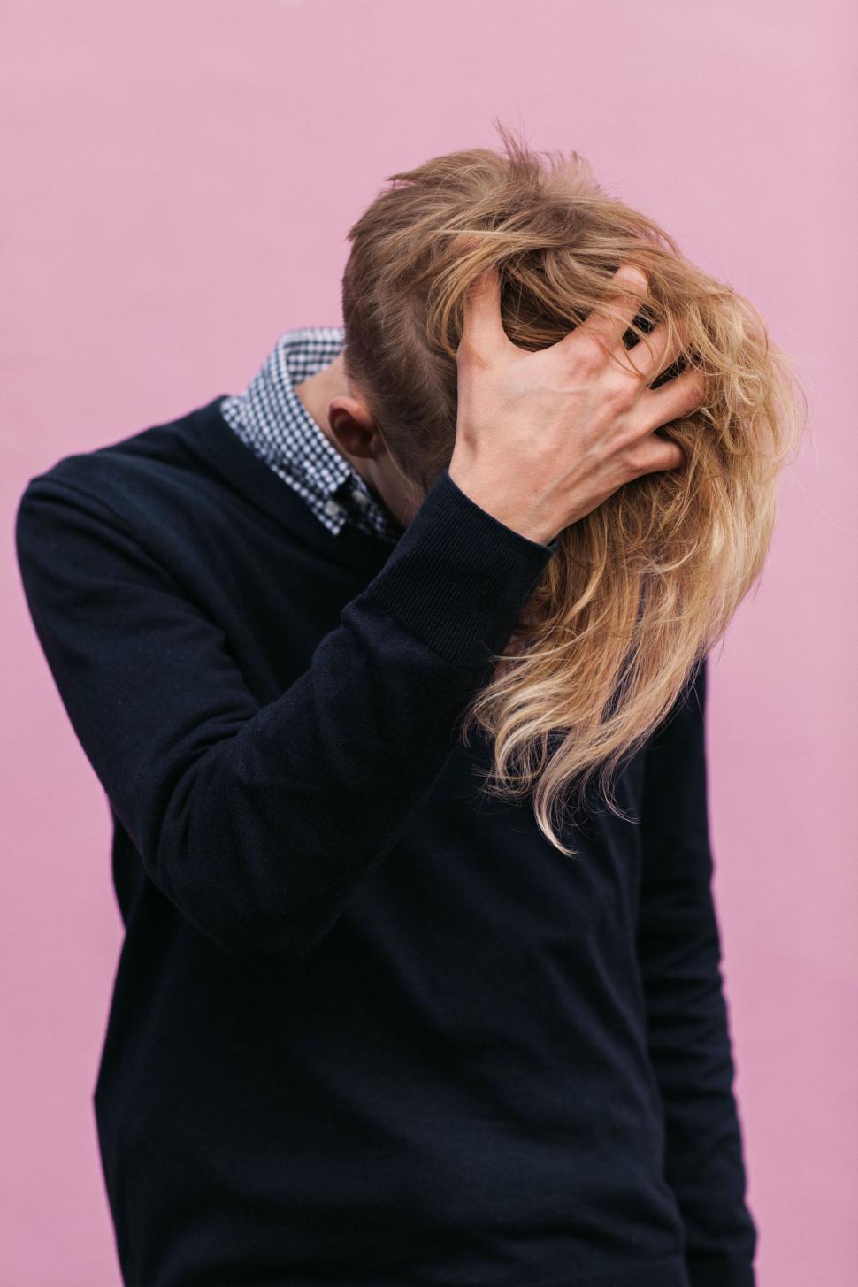 Free Image of Person grasping long blonde hair in front of pink background 