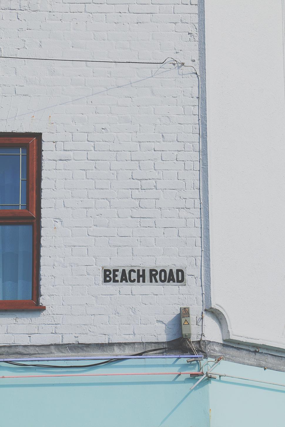 Free Image of Beach Road sign on a white brick wall with a window nearby 