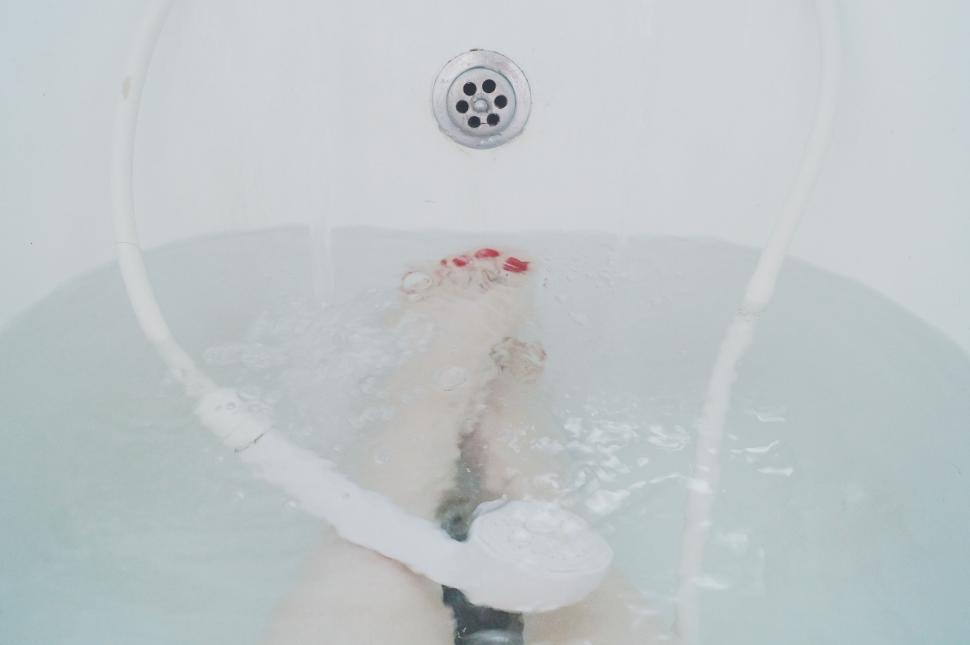 Free Image of Person soaking feet in water-filled bathtub with white showerhead 