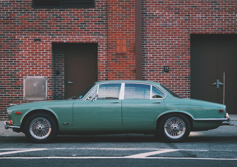 Free Image of Vintage green car parked beside a brick wall with two doors. 
