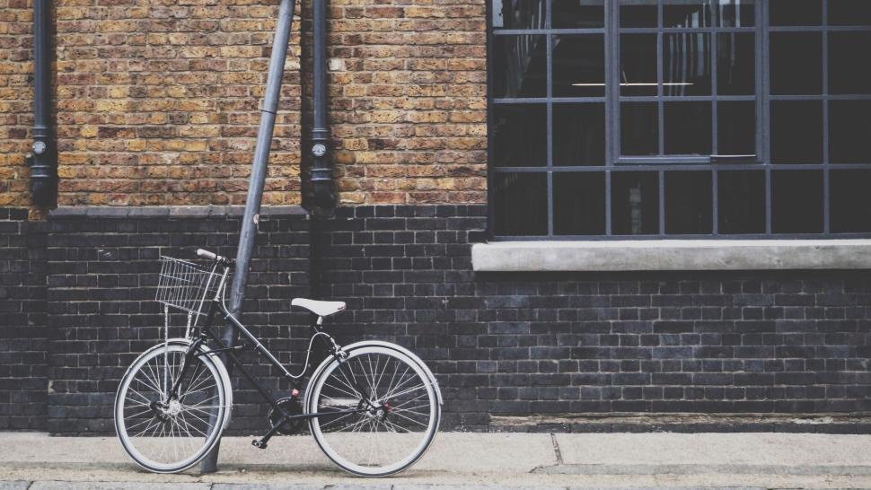 Free Image of Black bicycle with a basket parked next to a brick wall building. 