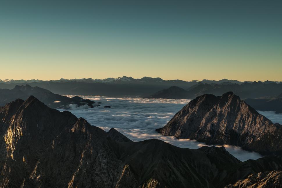 Free Image of Majestic mountain view with clouds beneath rugged peaks. 