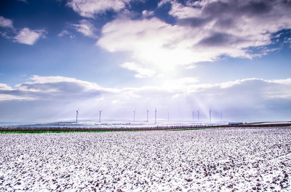 Free Image of Snow-covered fields with wind turbines under bright sky. 