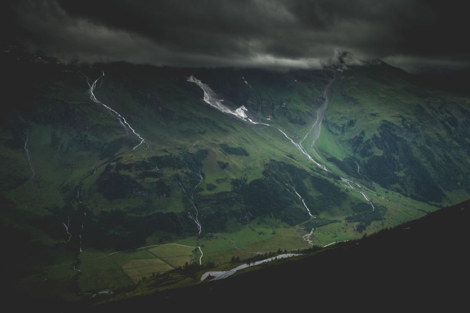 Free Image of Green mountains with winding rivers beneath a storm-filled sky. 